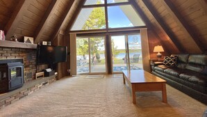 A cozy attic living room with a fireplace, a television, a leather sofa, and a large sliding glass door leading to a deck. - Four-season lakefront charm in Northern Michigan (Harbor Springs)