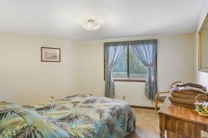 A bedroom with a bed, a window with curtains, a wooden dresser, and a framed picture on the wall.