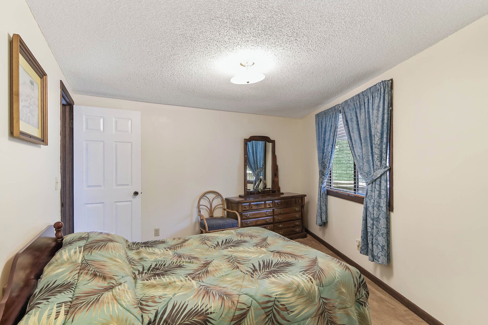 Quarto com cama, cômoda, cadeira, porta e janela com cortinas.