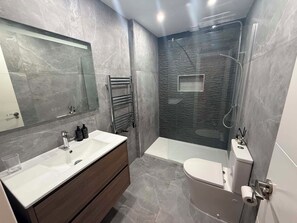 Et moderne badeværelse med vaskebord, spejl, bruser og toilet.