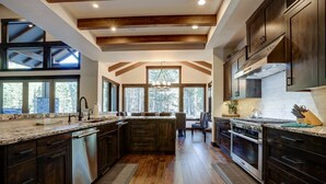 A spacious kitchen with dark wood cabinets, a large island, and a view of the outdoors through large windows. - Northwest Luxury with Access to Exclusive Golf (Sunriver)