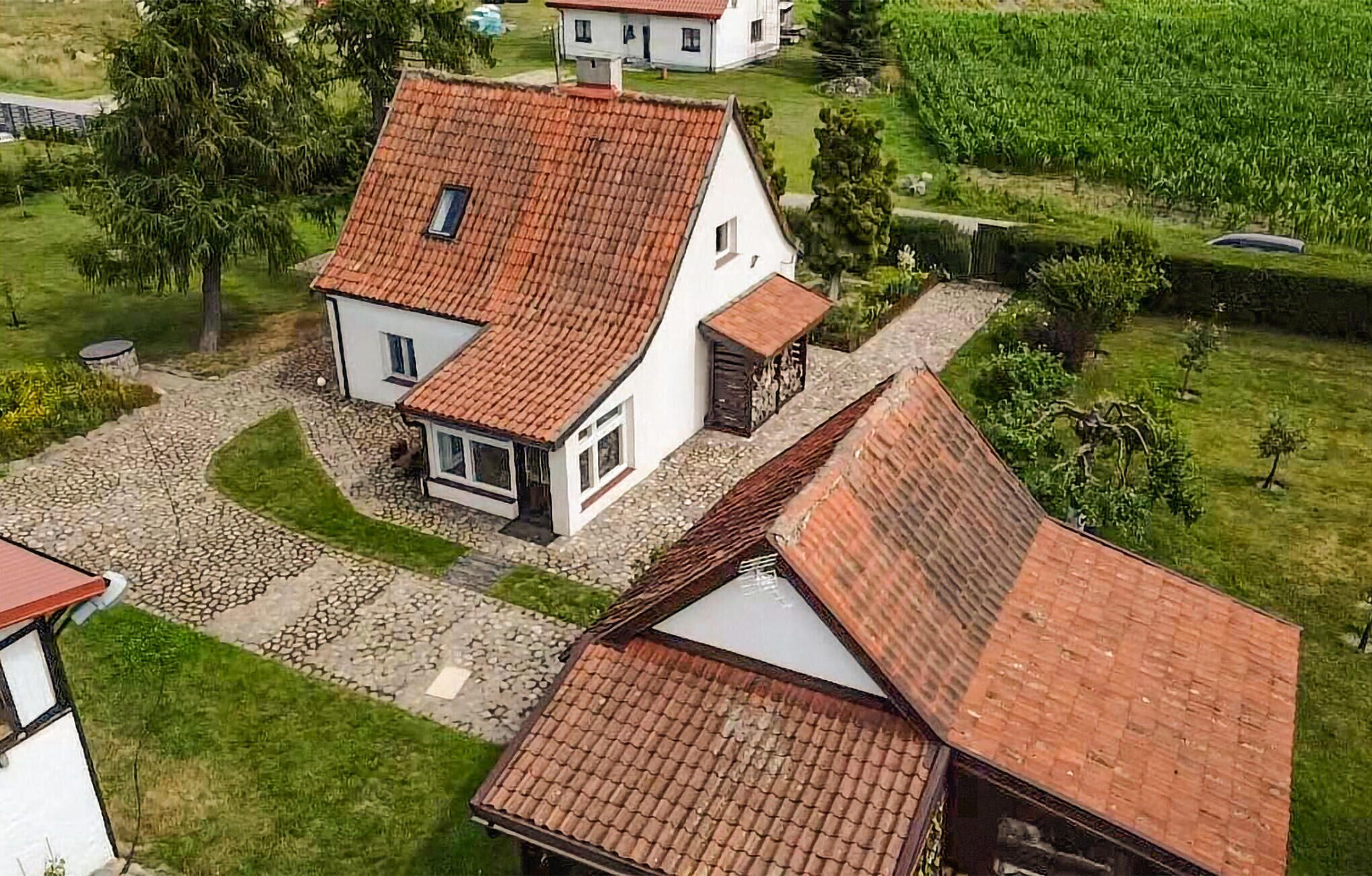 Une maison blanche avec un toit recouvert de tuiles rouges, une allée pavée de pierres et un jardin qui l’entoure.