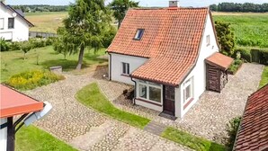 A two-story house with a red-tiled roof, a stone-paved driveway, and a small garden area.