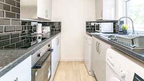 Una cocina moderna con encimeras negras, armarios blancos, horno empotrado, microondas y lavavajillas.