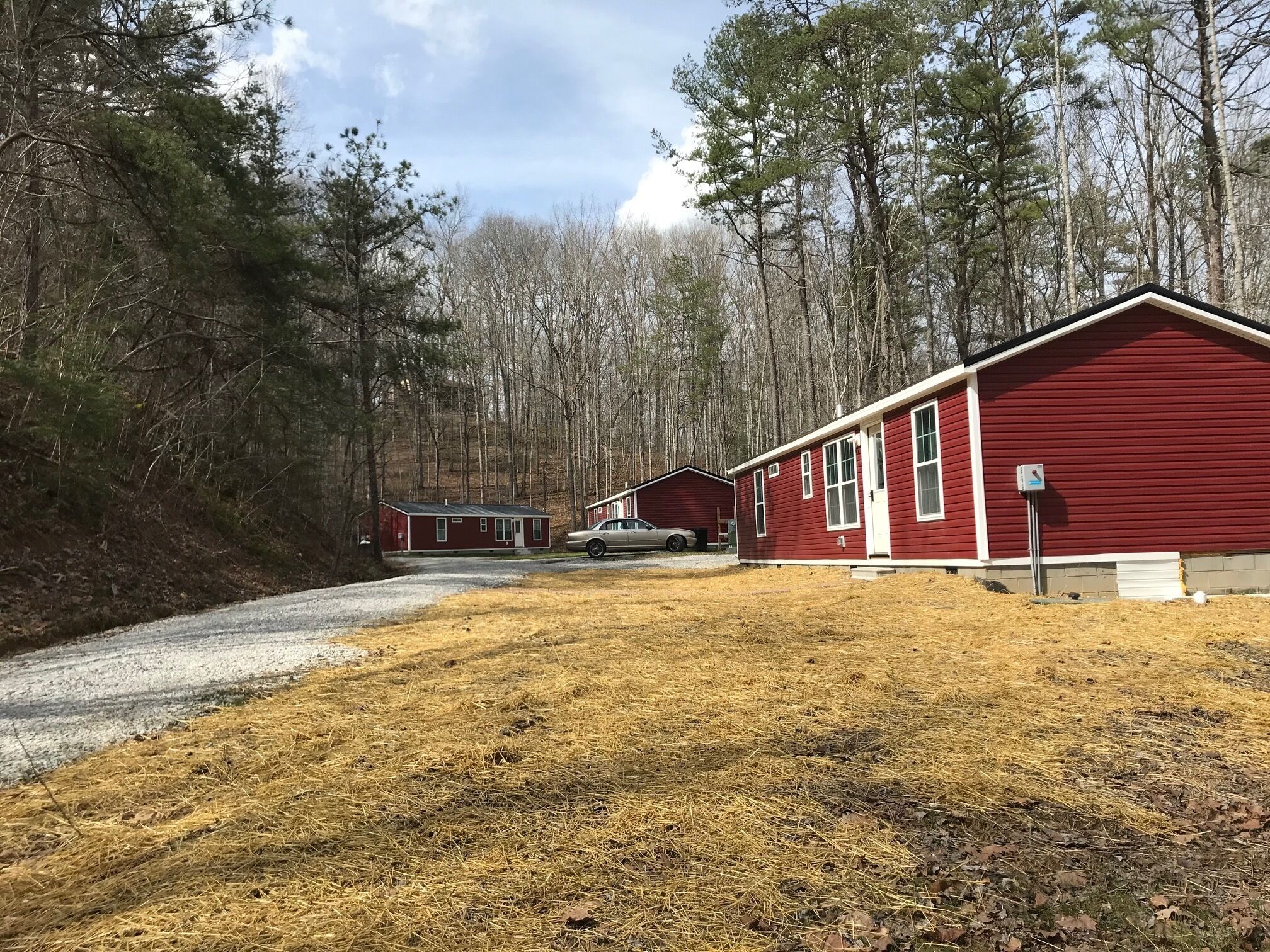 A row of red cabins with a gravel path leading to them, surrounded by trees.