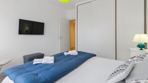 A hotel room with a bed, a TV mounted on the wall, a bedside table with a lamp, and a door leading to another room. - GuestHost - ⋆Inner City Suite⋆ a stone's throw from Piazza S.Oronzo! (Lecce)