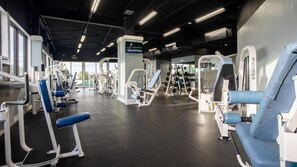 Un gimnasio con diversas máquinas de ejercicio, una pantalla de televisión y amplios ventanales.