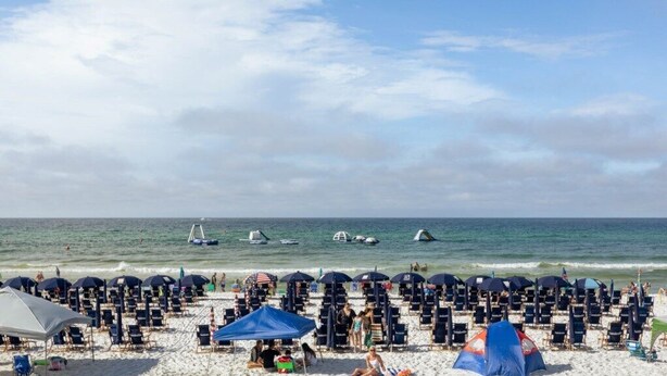 A beach with rows of sun loungers and umbrellas, a tent, and boats in the water.