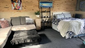 Een gezellige slaapkamer met een bank, een bed met beddengoed met een patroon, een klein nachtkastje met een plantje, en een schilderij aan de muur.