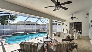 A covered outdoor area with a pool, wicker furniture, ceiling fans, and a patio table. - We Got You! Loaded home w/ Heated Pool & Large Yard (Fort Myers)