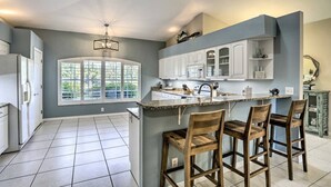 A modern kitchen with a large island, white cabinets, and a window providing natural light. - We Got You! Loaded home w/ Heated Pool & Large Yard (Fort Myers)