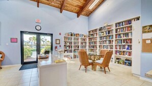 A library with a wooden ceiling, a reception desk, and multiple bookshelves filled with books. - SS 4224 2/2 Garden View Condo - Paradise Vacation Rental in Ocean Village (Fort Pierce)