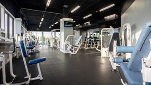 Ein Fitnessstudio mit verschiedenen Trainingsgeräten, einem Fernsehbildschirm und großen Fenstern.