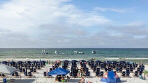 Ein Strand mit Liegestühlen, Sonnenschirmen, einem Zelt und Booten im Wasser.