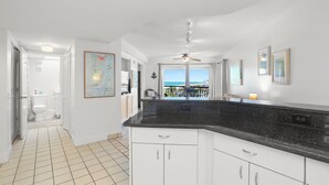 A modern kitchen with white cabinets, a black countertop, and a ceiling fan. - 🌴 Gulf View Condo — Gulf Strand Resort, St. Pete Beach (St Pete Beach)