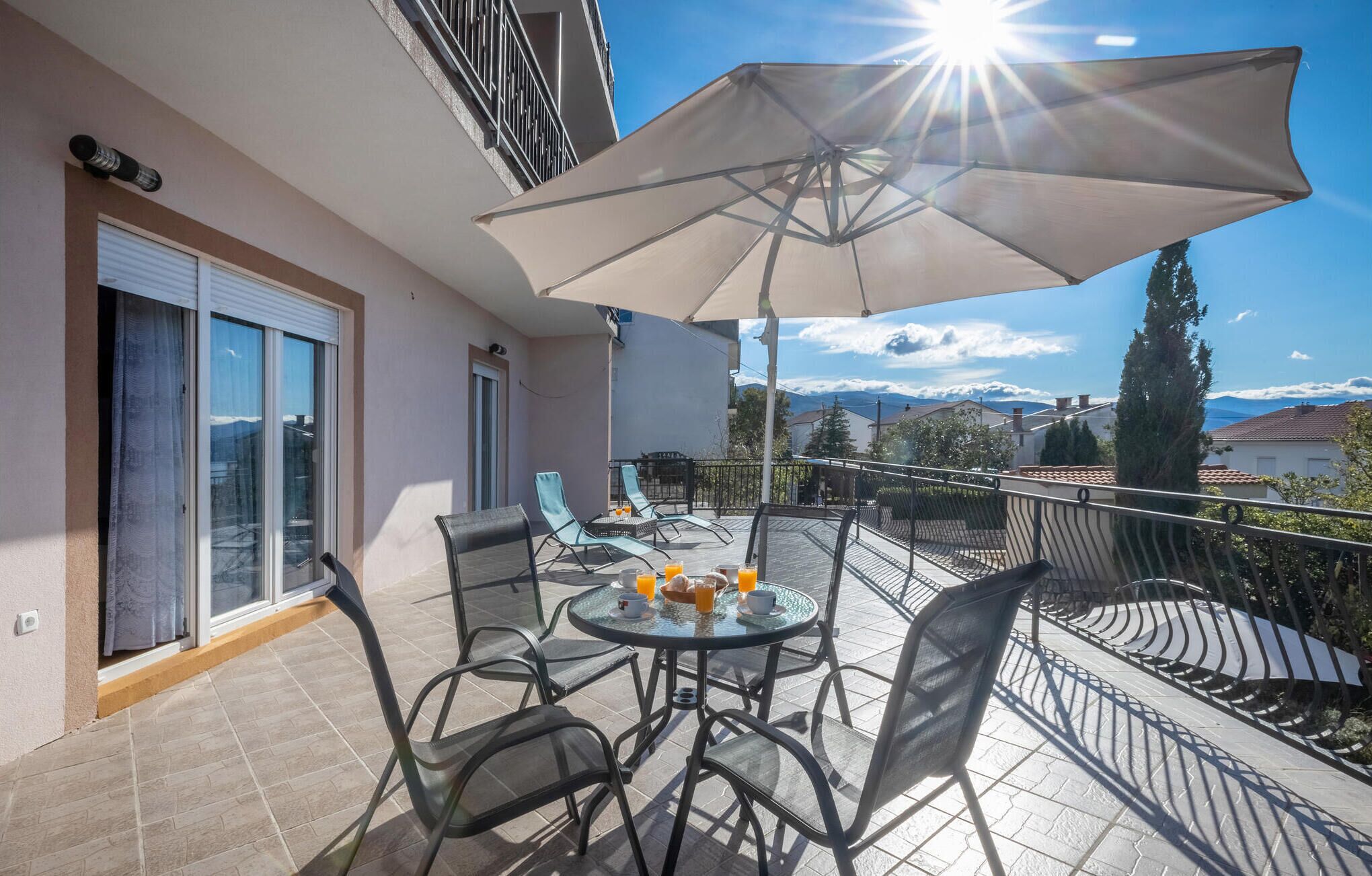 Uma varanda com mesa, cadeiras e guarda-sol.