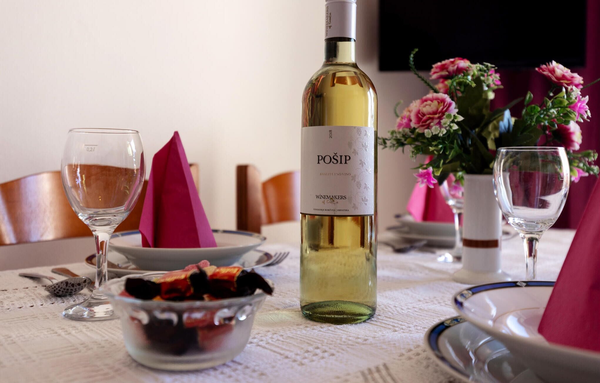 A dining table set with wine glasses, a bottle of wine, and a bowl of food.