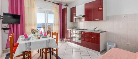 A modern kitchen with red cabinets, a dining area with a table set for two, and a TV mounted on the wall.