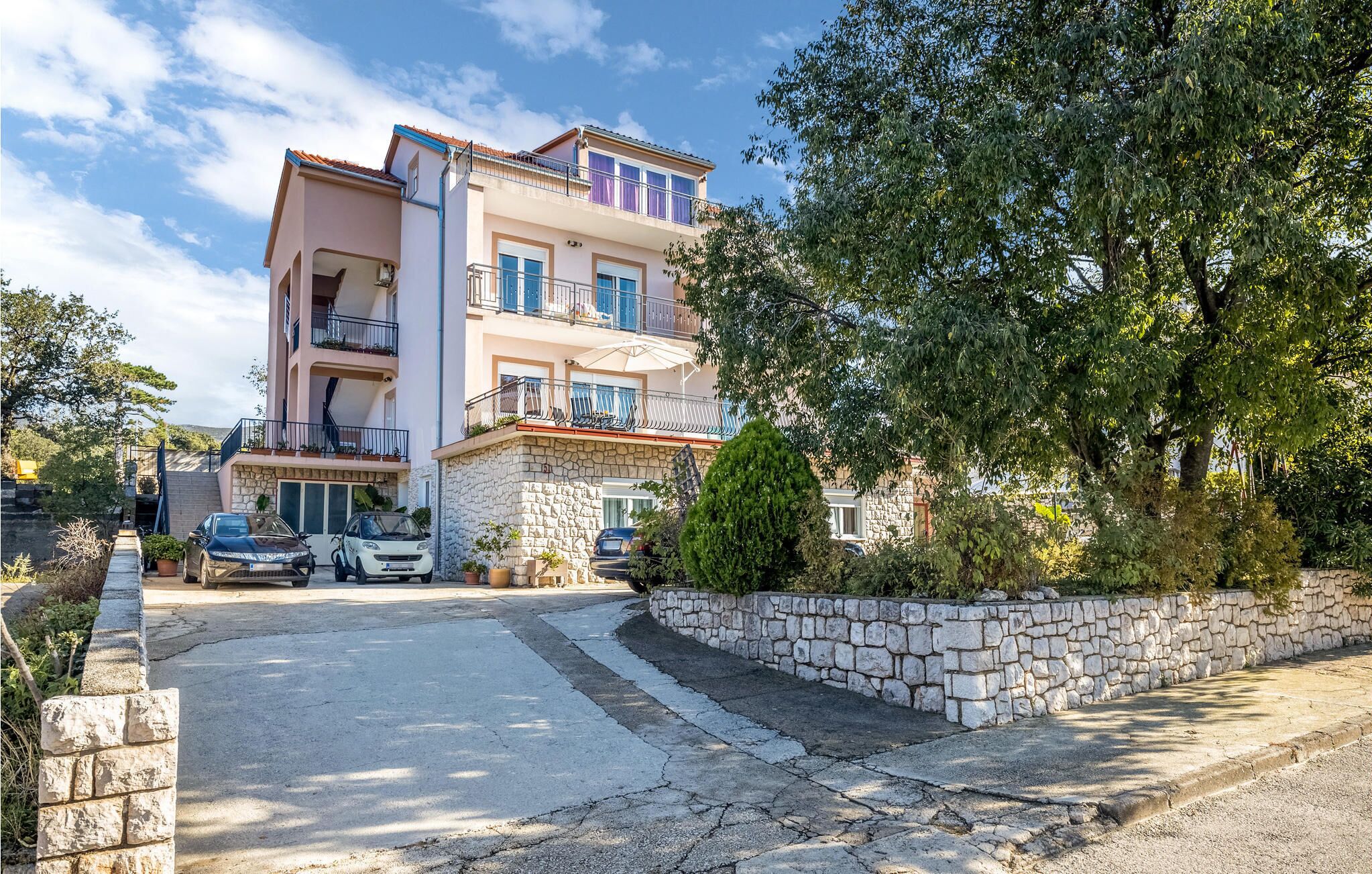 A multi-story residential building with balconies, a stone facade, and a paved driveway.