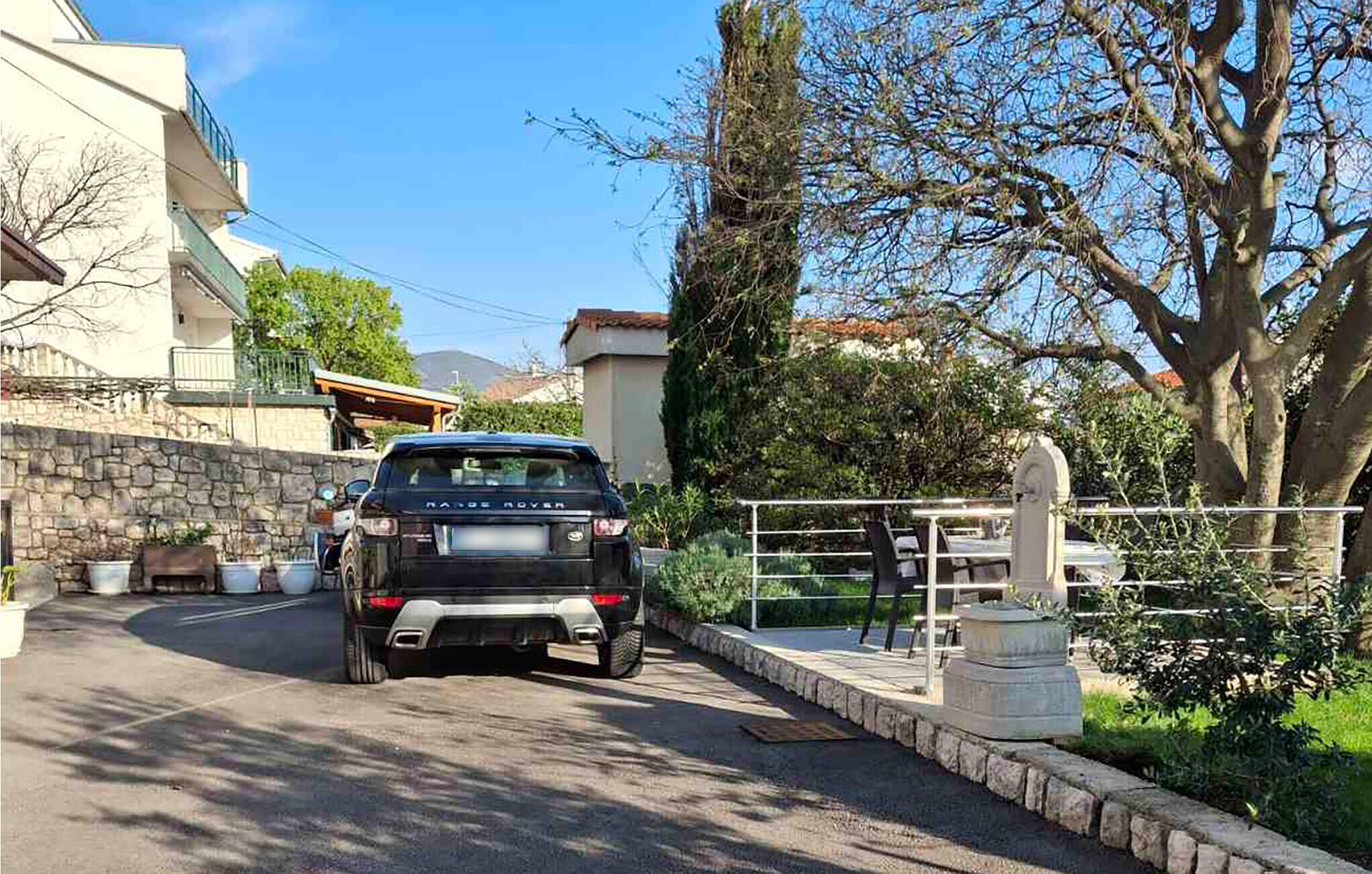 Ein schwarzer Range Rover steht auf einer Wohnstraße mit Steinmauern, einer Steinsitzbank und einer Statue im Hintergrund.