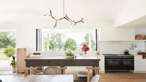 Una cocina moderna con un gran ventanal, una mesa de madera y una lámpara colgante original.