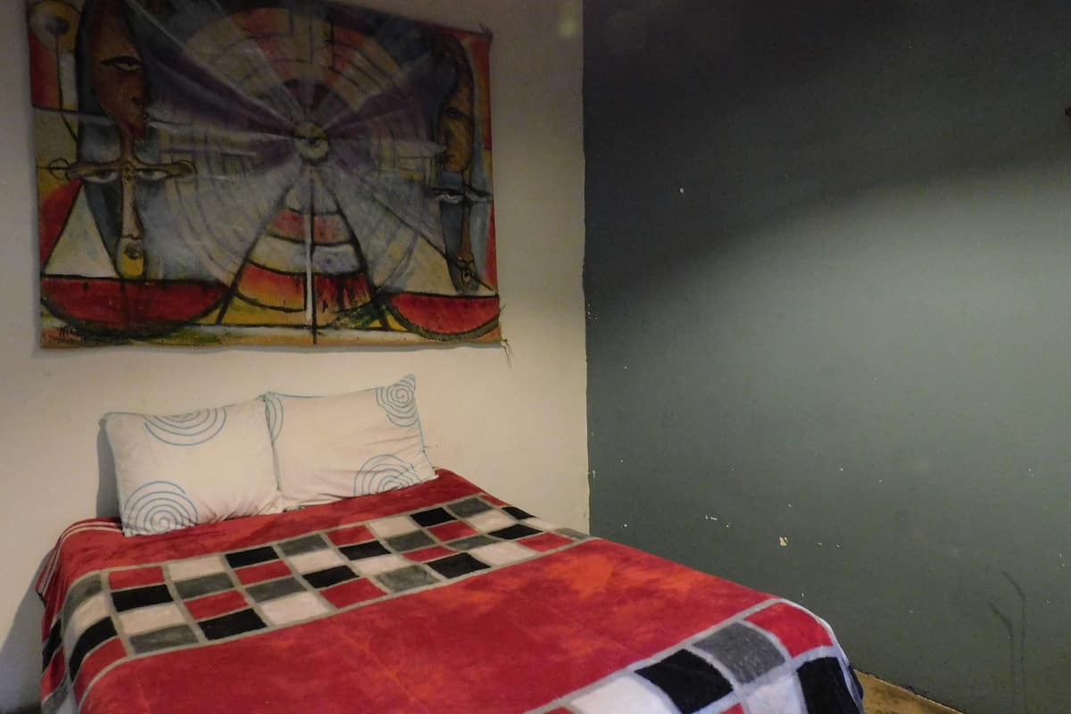 A bedroom with a bed, a colorful abstract painting on the wall, and a checkered blanket.