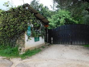 A rustic building with a metal gate, surrounded by lush greenery and a gravel path. - San Nicolás Rotamundos (San Cristóbal de las Casas)