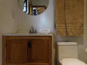 A bathroom with a wooden cabinet, a sink with a faucet, a toilet, and a towel hanging on the wall. - San Nicolás Rotamundos (San Cristóbal de las Casas)