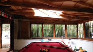 A pool table with balls and cues, wooden beams, and large windows with bamboo outside. - San Nicolás Rotamundos (San Cristóbal de las Casas)