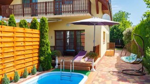 Una casa de dos pisos con piscina, mobiliario exterior y una silla colgante.