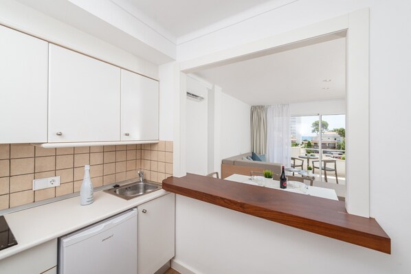 A modern kitchen with white cabinets, a wooden countertop, and a view of an outdoor balcony with a table and chairs. - MASSANET (2C) - Luminous and modern apartment with a terrace, located just 250 meters from (Canyamel)