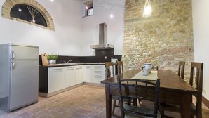 A kitchen with a stone wall, a built-in oven, and a dining table with chairs.