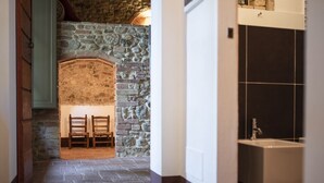 A stone-walled hallway leading to a bathroom with a sink and a chair.