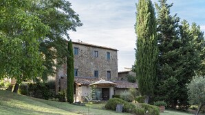 A stone building with a tiled roof, surrounded by trees and a well-maintained lawn.