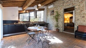 A rustic kitchen with stone walls, wooden beams, and a dining area with metal chairs and a table.