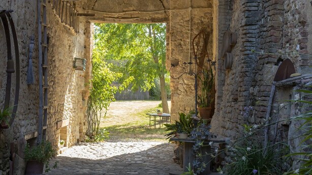 A stone pathway leading to an outdoor seating area with tables and chairs, surrounded by potted plants and a rustic stone wall.