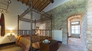 A four-poster bed in a stone-walled room with a wooden ceiling and a small table with a lamp. - PICCIONAIA - country home with garden in the heart of Chianti - 2 persons (Montespertoli)