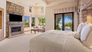 Un dormitorio amplio con una cama grande, una chimenea, un televisor y vistas al exterior.