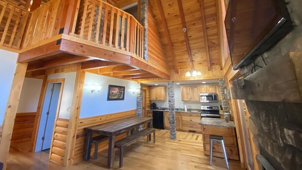 L’intérieur d’un chalet rustique, avec une terrasse en bois, des piliers en pierre, une cuisine équipée d’appareils modernes et une cheminée.