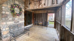 Une terrasse en bois avec un banc et des chaises, un mur de pierres orné d’une guirlande, et, au loin, une vue sur une cabane en bois.