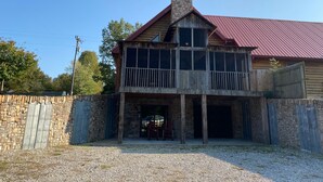 Une cabane en rondins à deux étages, avec des fondations en pierre, un toit en métal rouge et une allée gravillonnée.