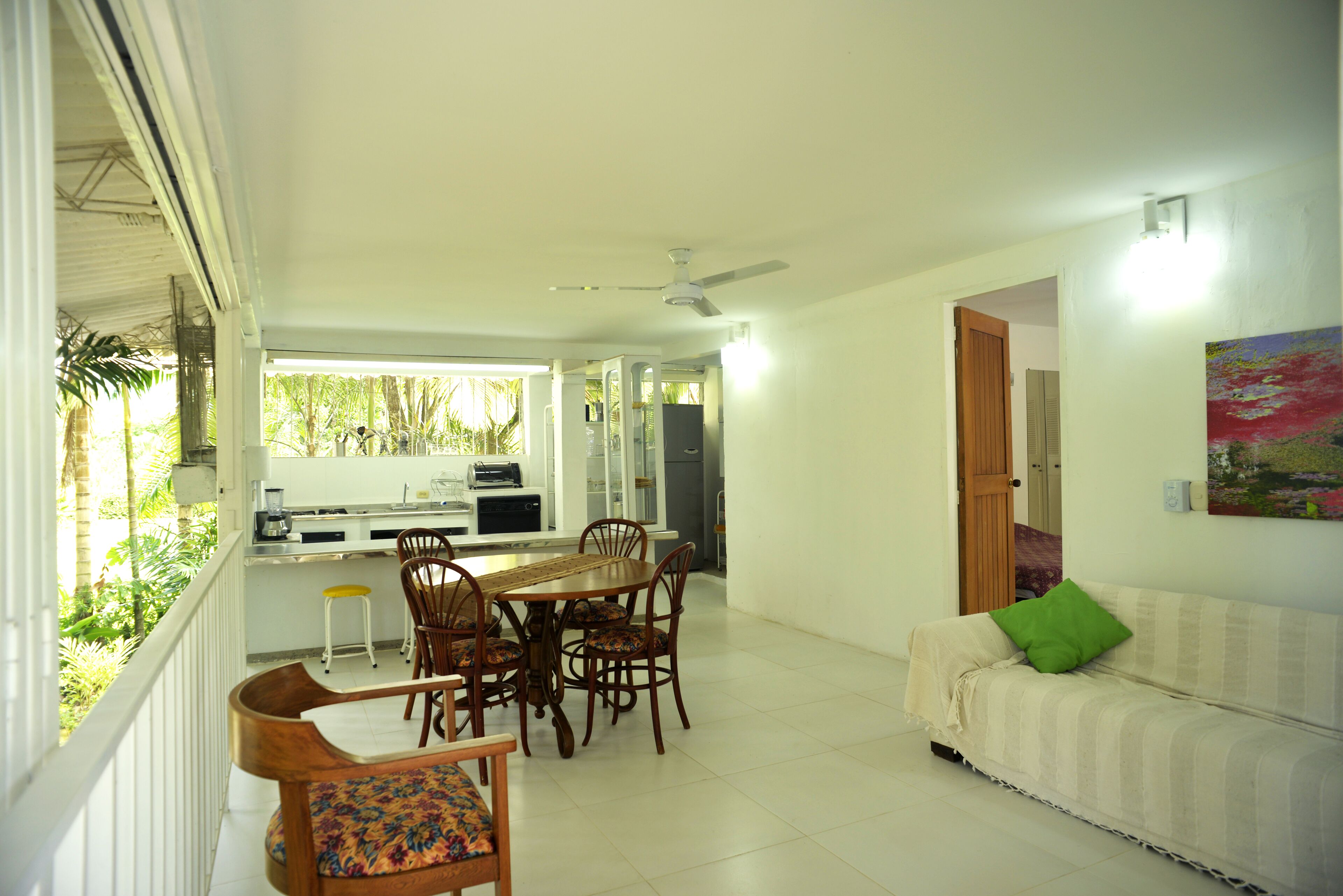 Un amplio espacio habitable con una mesa de comedor y sillas, un sofá con un cojín verde y una cocina al fondo.