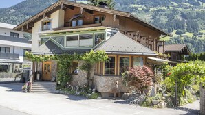 Un edificio in legno a due piani con un balcone, facciata in pietra e vista su un paesaggio montuoso.