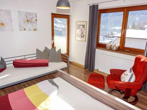 A cozy room with a bed, a red chair, a window with a view of snow-covered mountains, and a radiator.