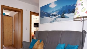 Un canapé gris avec des coussins bleus, une porte en bois et un tableau représentant un paysage de montagne enneigé.