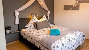 Une chambre à coucher avec un lit à baldaquin, des lampes de chevet, une table de chevet, une plante en pot et du linge de lit orné de motifs en forme d’étoiles.
