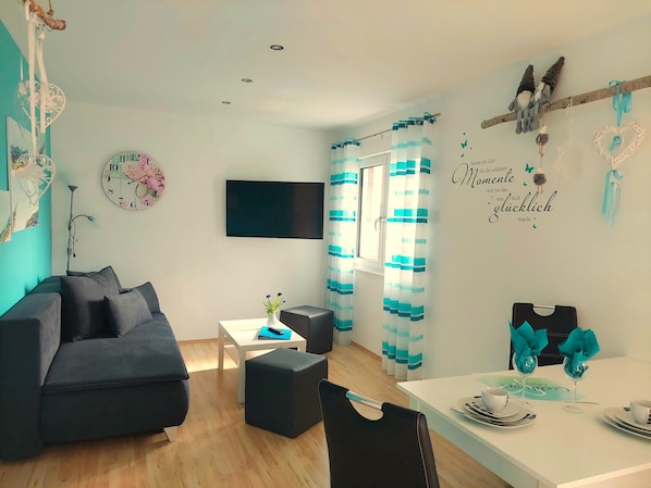 Ein modernes Wohnzimmer mit einer Couch, einem Fernseher, einer Uhr und einem Essbereich mit Tisch für zwei Personen.