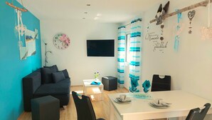 Un salon moderne avec un canapé, une table à manger et des chaises, un téléviseur et une horloge murale.