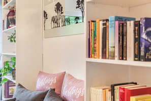 A bookshelf with books, a teddy bear, and a wall art piece.