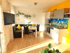 A modern kitchen with a microwave, oven, and sink, a dining area with a table and chairs, and a living area with a sofa and a TV. - Apart Diana - new vacation home - App. “Rossberg” with Mountain View, Wi-Fi & Balcony (Vils)